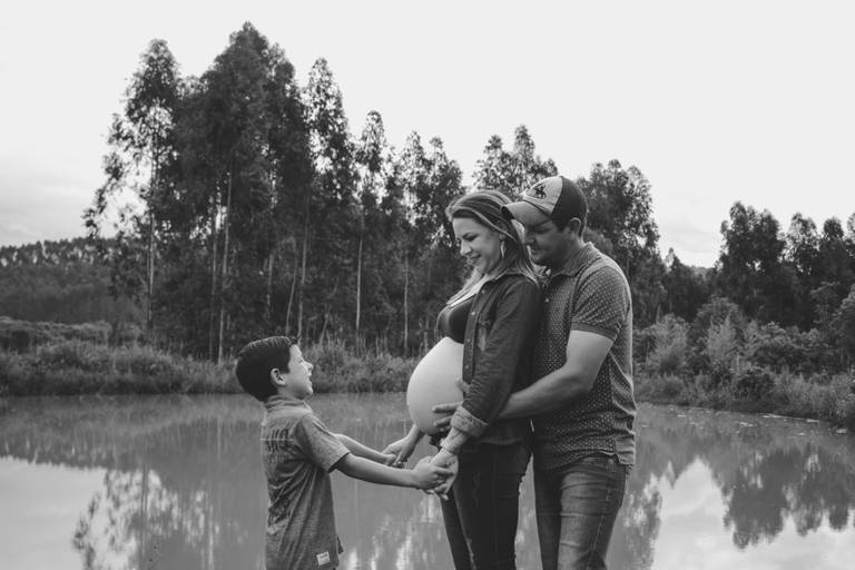 família unida em ensaio de gestante em frente de um lago e floresta de eucaliptos