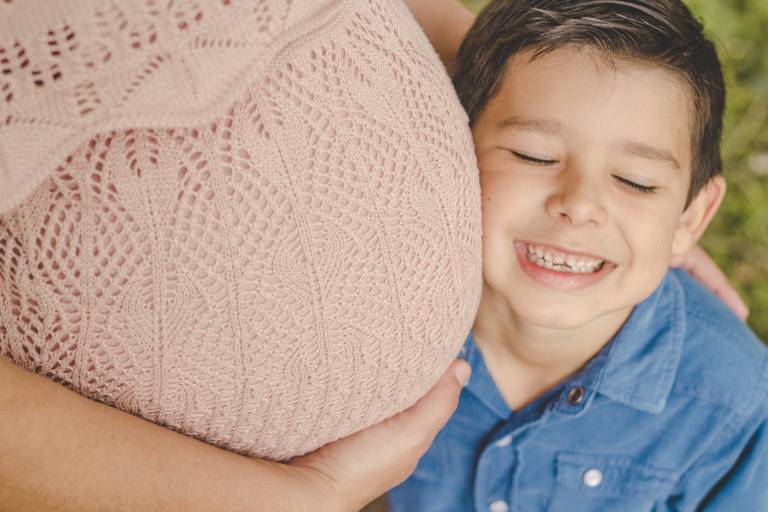 filho mais velho sorrindo ao lado da barriga da mamãe em ensaio gestante