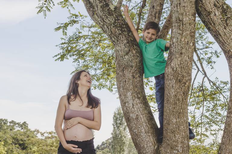 gravida sorrindo para filho em cima da árvore no anila em sessão de fotos 