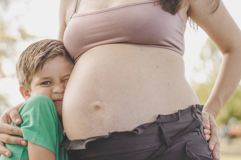 irmão mais velho colado na barriga da mãe fazendo careta fofa