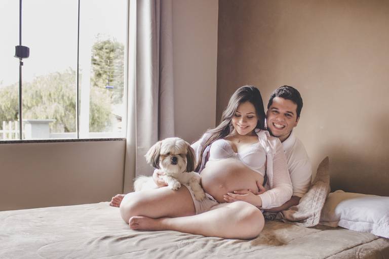 casal em fotos em casa com cachorro sobre a cama durante sessão gestante