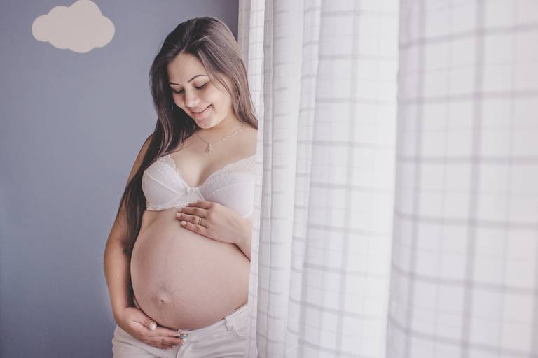gestante de lingerie em ensaio em casa no quarto do bebe ao lado da janela