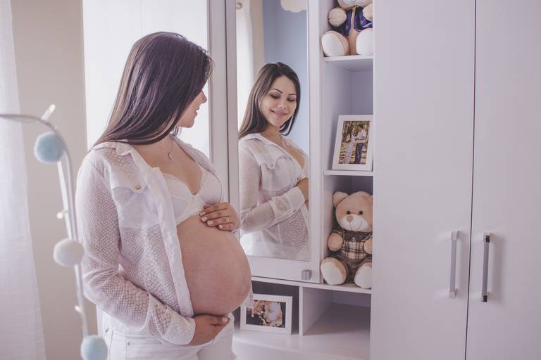 mãe gestante se admirando em espelho do quartinho do bebê 