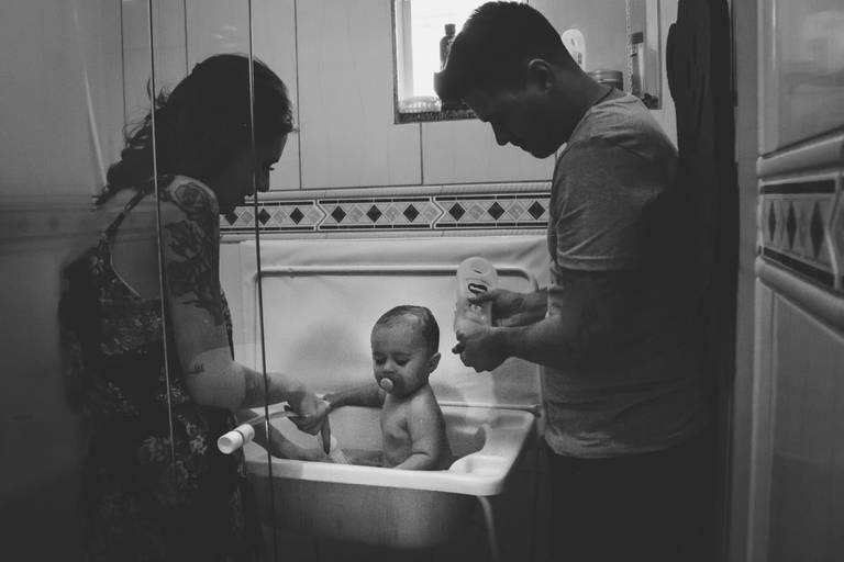 pais dando banho em bebe no banheiro de casa durante sessão de fotos