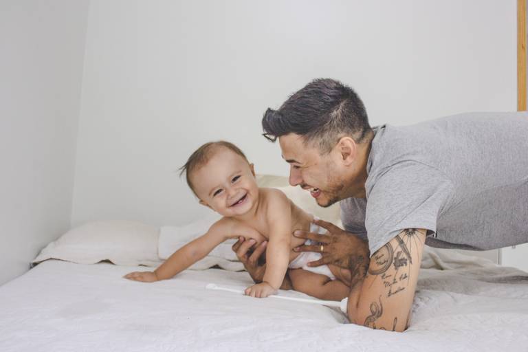 bebe e papai sorrindo sobre a cama