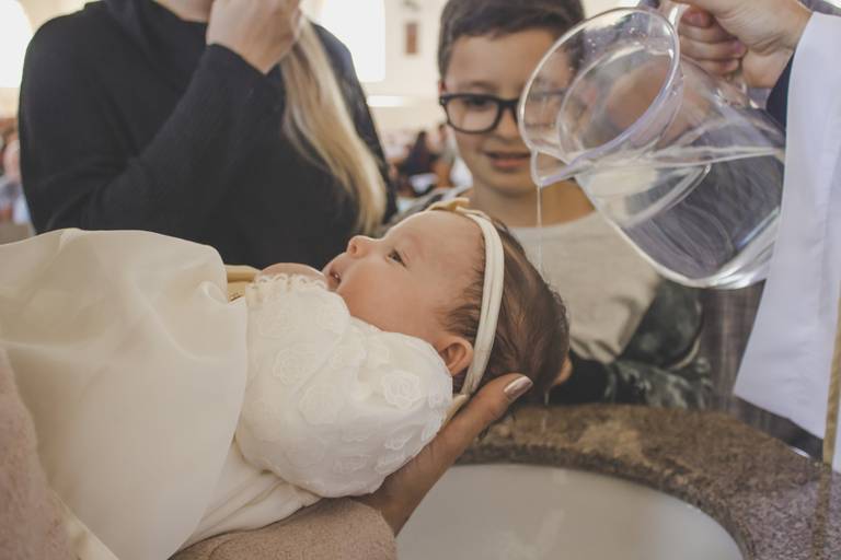 foto do momento em que a bebe é batizada com aguá santa