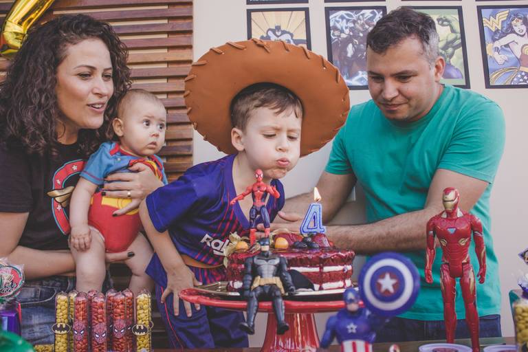 Criança soprando a vela no seus quatro anos em aniversario de super heróis em casa
