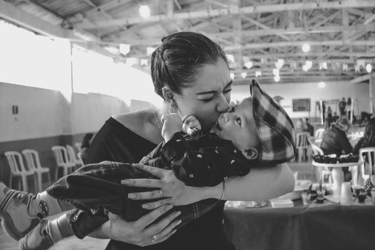 foto em preto e branco de madrinha beijando afilhado sobre seu colo em festa infantil
