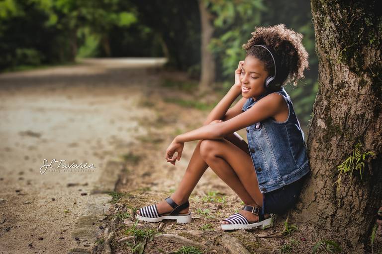 Menina sentada no pé da árvore ouvindo música. Fotografia infantil no bosque da barra.