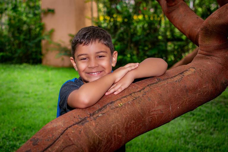 Menino sorridente encostado na árvore no rio 2 park