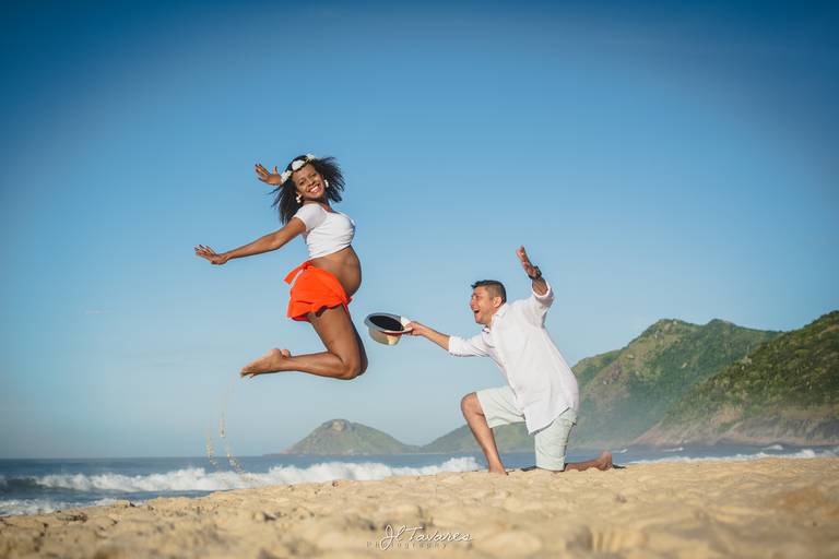 ensaio gestante criativo com a grávida pulando e o pai fazendo pose de sambista ajoelhado com chapéu panama.