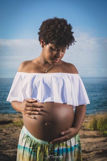 Mulher Negra Grávida na praia de grumari croped branco e saia estampada azul, verde e amarela na praia do secreto, Rio de Janeiro.