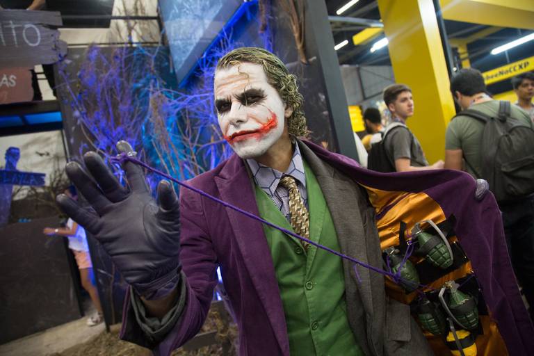 Pessoa vestindo cosplay detalhado do Coringa em uma feira, com foco na caracterização e na performance do personagem.