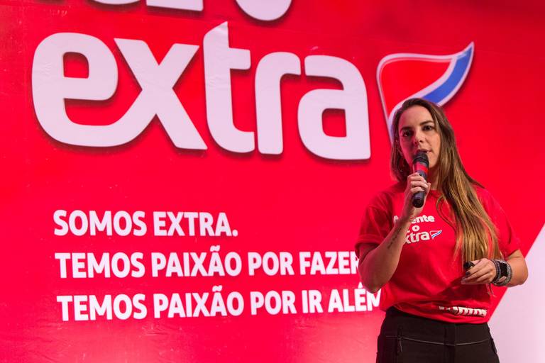 Palestrante falando no palco, com um painel de apresentação visual ao fundo, que complementa sua fala.