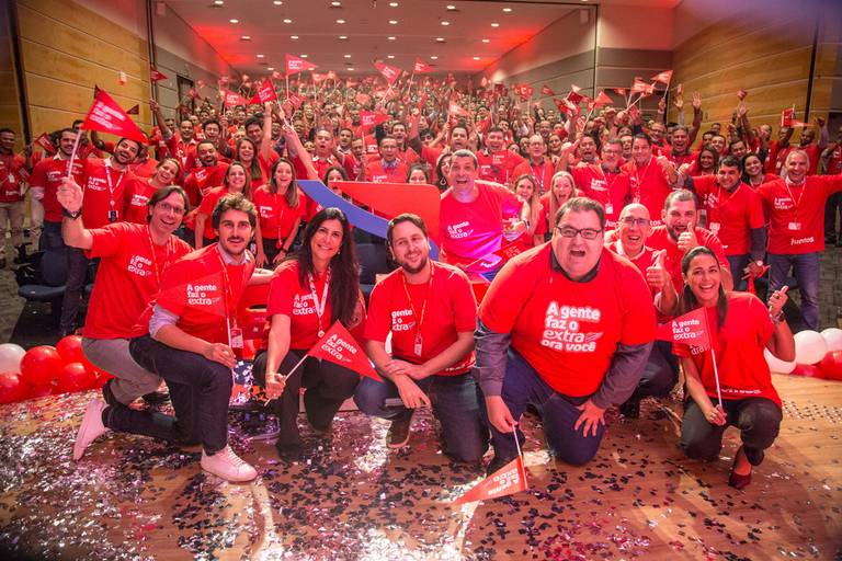 Foto posada de palestrantes no palco, com o público ao fundo, criando uma imagem que representa a conexão entre os apresentadores e a audiência.