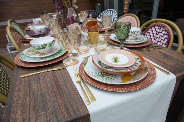 Mesa de evento elegantemente decorada com louças finas e de design, realçando a sofisticação do ambiente.