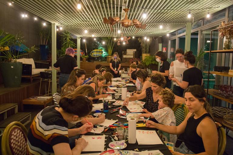 Outra vista da mesa de participantes de um workshop, com rascunhos ou trabalhos em andamento, mostrando a interação com os materiais.