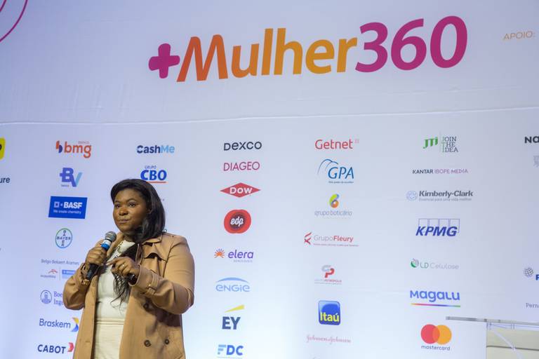 Palestrante em um momento de clímax da fala, com microfone e projeção de tela ao fundo.