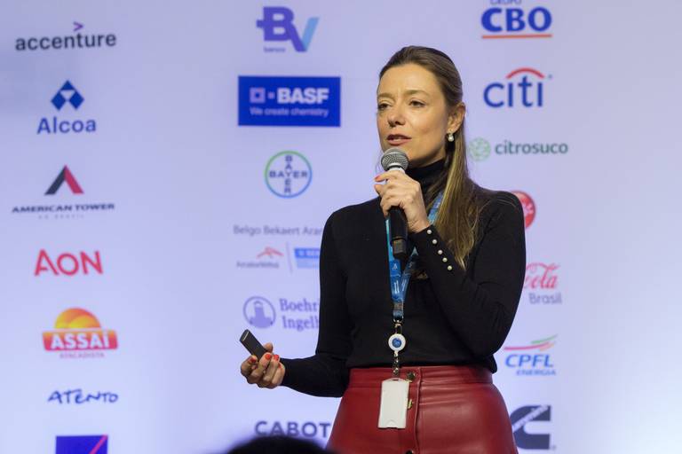 Palestrante no palco, com microfone em mãos, expressando-se com clareza durante sua fala.
