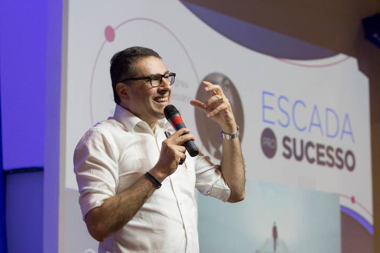 Palestrante gesticulando enquanto fala no palco, transmitindo dinamismo à apresentação.