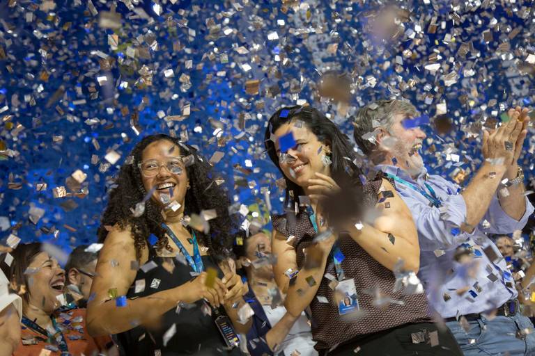 Participantes de um evento comemorando sob uma chuva de papéis picados, em um momento de euforia e alegria