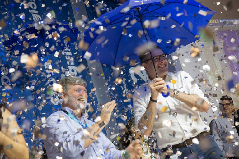 Grupo de participantes festejando em meio a uma cascata de confetes ou papéis, capturando a energia do evento.