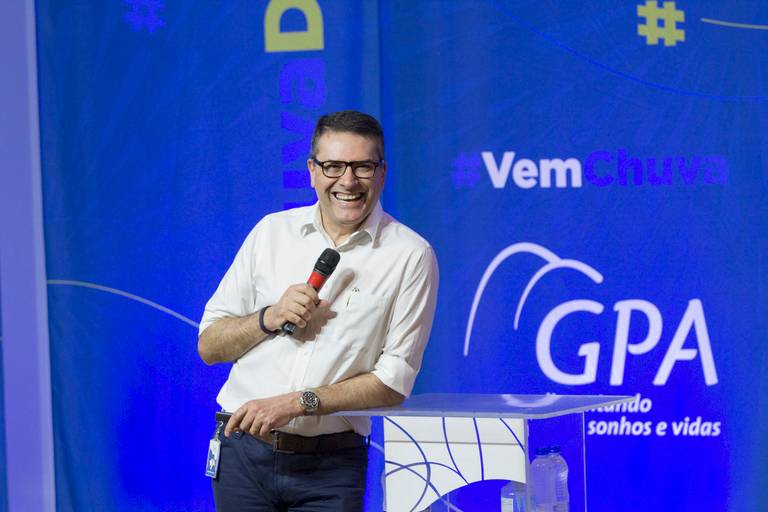 Palestrante em destaque no palco, falando ao microfone com expressão engajada.