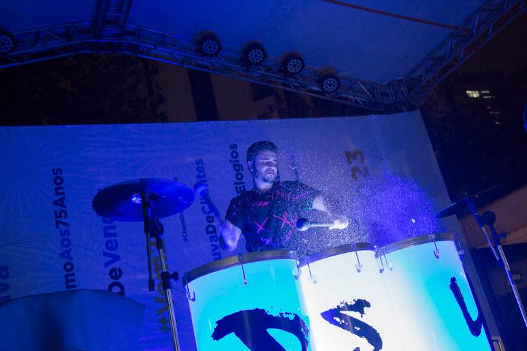 Artistas se apresentando em um show de tambores, com energia e movimento, no palco do evento.