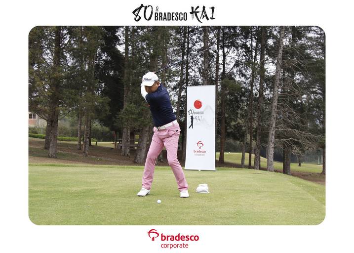 Jogador de golfe em movimento, batendo na bola com o taco, com foco na técnica e na concentração.