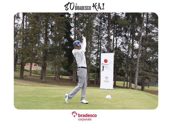 Outro ângulo de um jogador de golfe realizando a tacada, com a bola em voo e a paisagem do campo ao fundo.