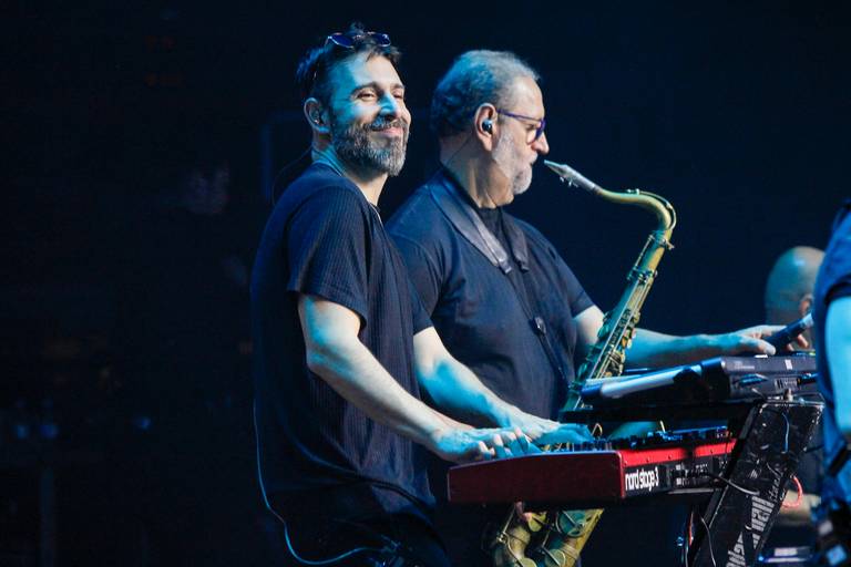 Músicos se divertindo enquanto tocam seus instrumentos no palco, transmitindo a energia e alegria da performance.