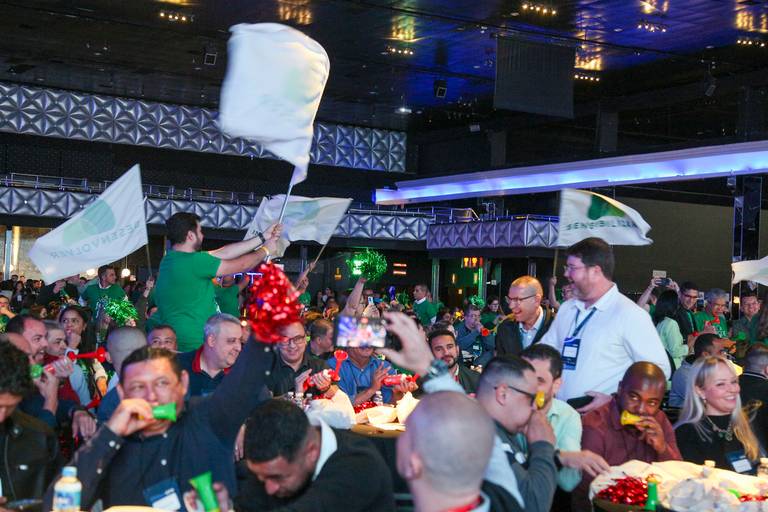 Participantes de um evento balançando bandeiras com entusiasmo, criando uma atmosfera vibrante na plateia.