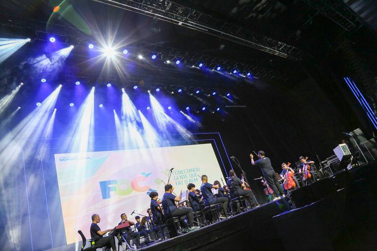 Músicos se apresentando no palco com seus instrumentos, criando um ambiente de show em um evento.