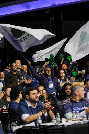 Público em massa balançando bandeiras com entusiasmo, criando uma cena de grande energia e participação em um evento.