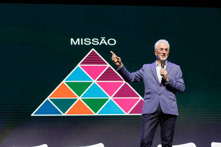 Palestrante apontando para um telão ou slide em sua apresentação, direcionando a atenção do público.