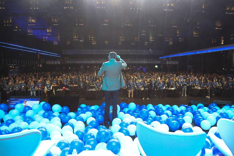 Diretor da empresa falando, com o público ao fundo, demonstrando a comunicação da liderança com os colaboradores.