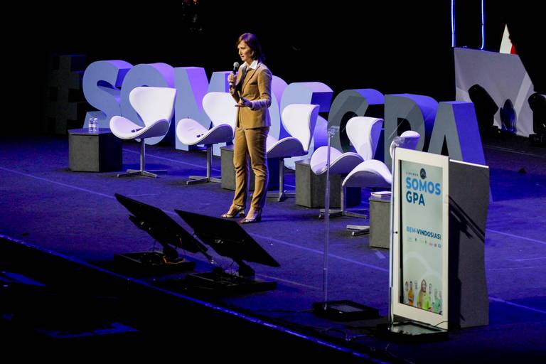 Palestrante no palco, utilizando microfone e possivelmente um telão, durante uma apresentação em evento.