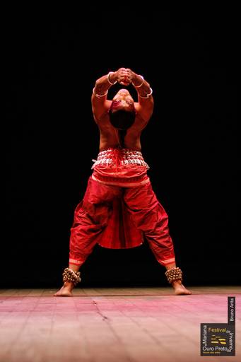 Homem dançando com energia em um espetáculo, com movimentos expressivos e foco na sua performance artística.