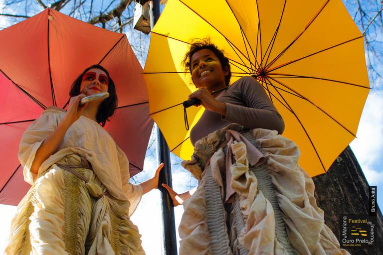 Duas artistas segurando sombrinhas coloridas, adicionando um elemento visual vibrante à sua performance ou presença em um evento.