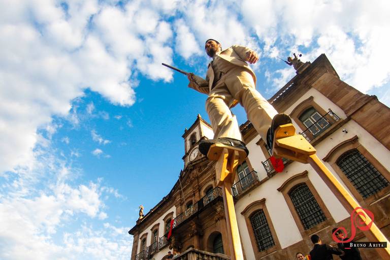 Artista em perna de pau, com figurino e postura que demonstram equilíbrio e presença em um evento cultural.