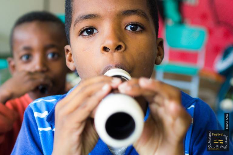 Menino tocando flauta em ambiente escolar, demonstrando concentração e aprendizado musical.