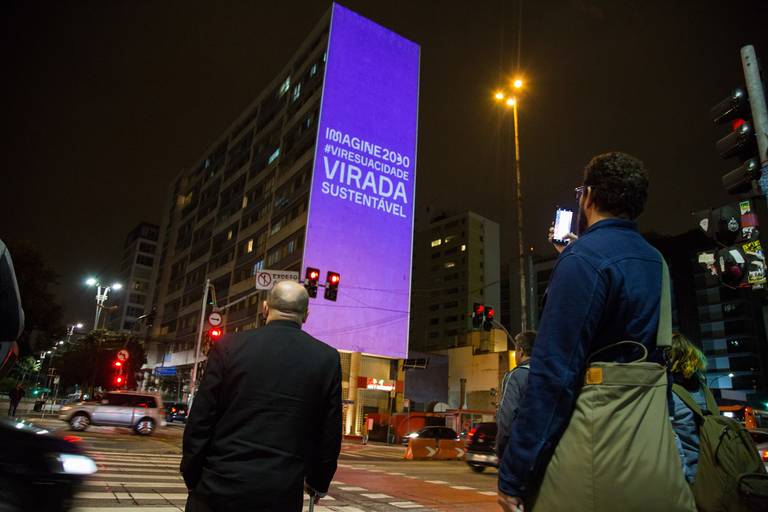 Pessoas observando uma projeção artística em um prédio, interagindo com a instalação visual urbana.