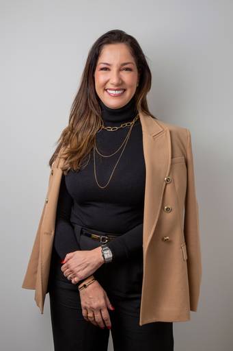 Retrato de Mulher com blazer apoiado nos ombros, em pose amigável, segurando as mãos. Traje preto e acessórios discretos. (Retrato Profissional, São Paulo, Fotógrafo Bruno Arita)