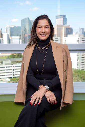 Mulher sentada próxima à janela, com blazer preto nos ombros, em um retrato que usa a vista da cidade de São Paulo como cenário. (Retrato Profissional, São Paulo, Fotógrafo Bruno Arita)