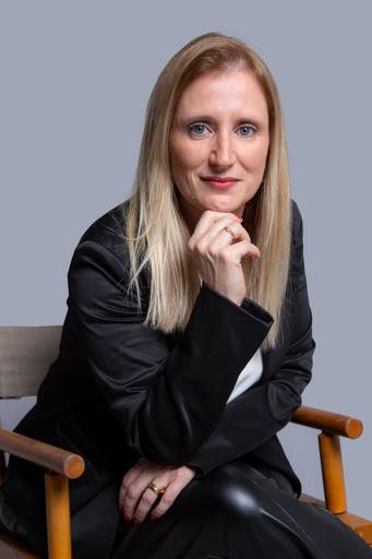 Mulher em retrato de negócios, com olhar perspicaz e postura profissional em fundo neutro.