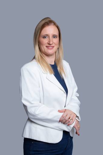 Profissional feminina em retrato, com postura assertiva e presença forte em ambiente corporativo com fundo discreto.