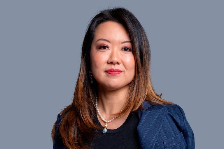 Mulher em retrato corporativo, com semblante sério e postura que denota liderança em fundo discreto.