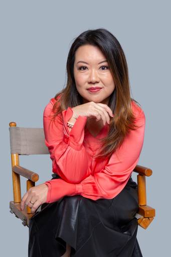 Retrato de uma profissional feminina, com expressão pensativa e postura firme em fundo neutro.