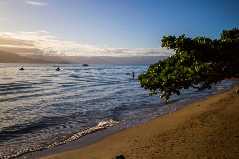 Mar iluminado pelos tons alaranjados e rosados do pôr do sol em Ilhabela, São Paulo, com o horizonte visível.