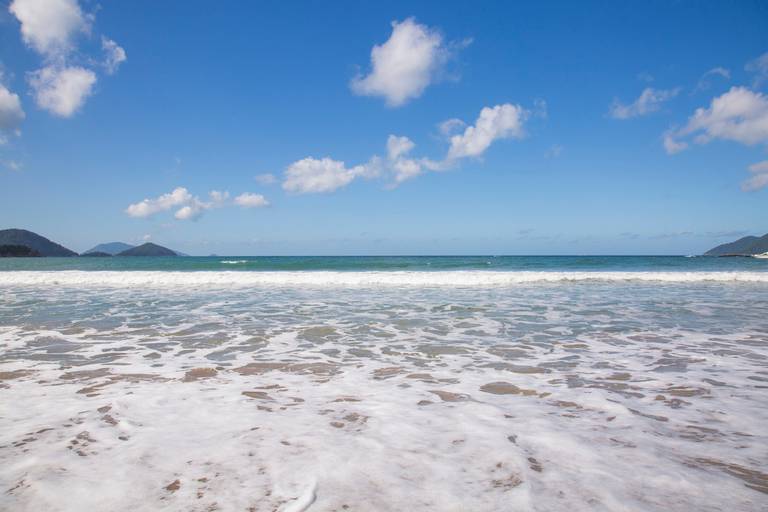 Cena da Praia de Castelhanos em Ilhabela, São Paulo, com ondas suaves e a linha da costa.
